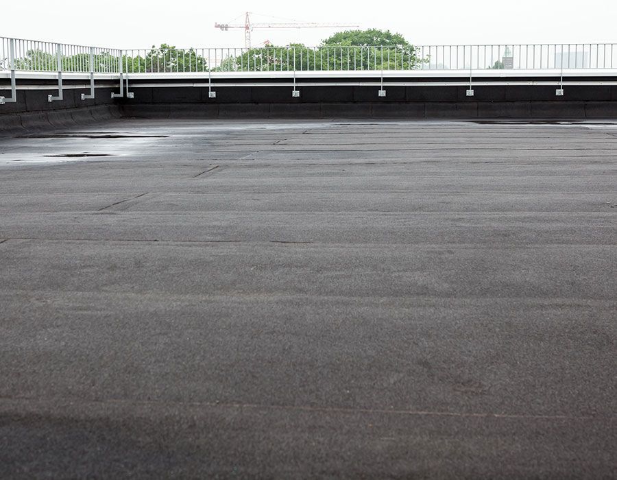A flat, black-surfaced rooftop with a metal railing along the perimeter under a cloudy sky.