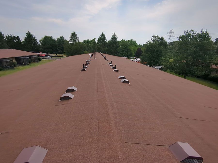 A long, flat, brown industrial roof featuring multiple ventilation covers in a line under a cloudy sky.
