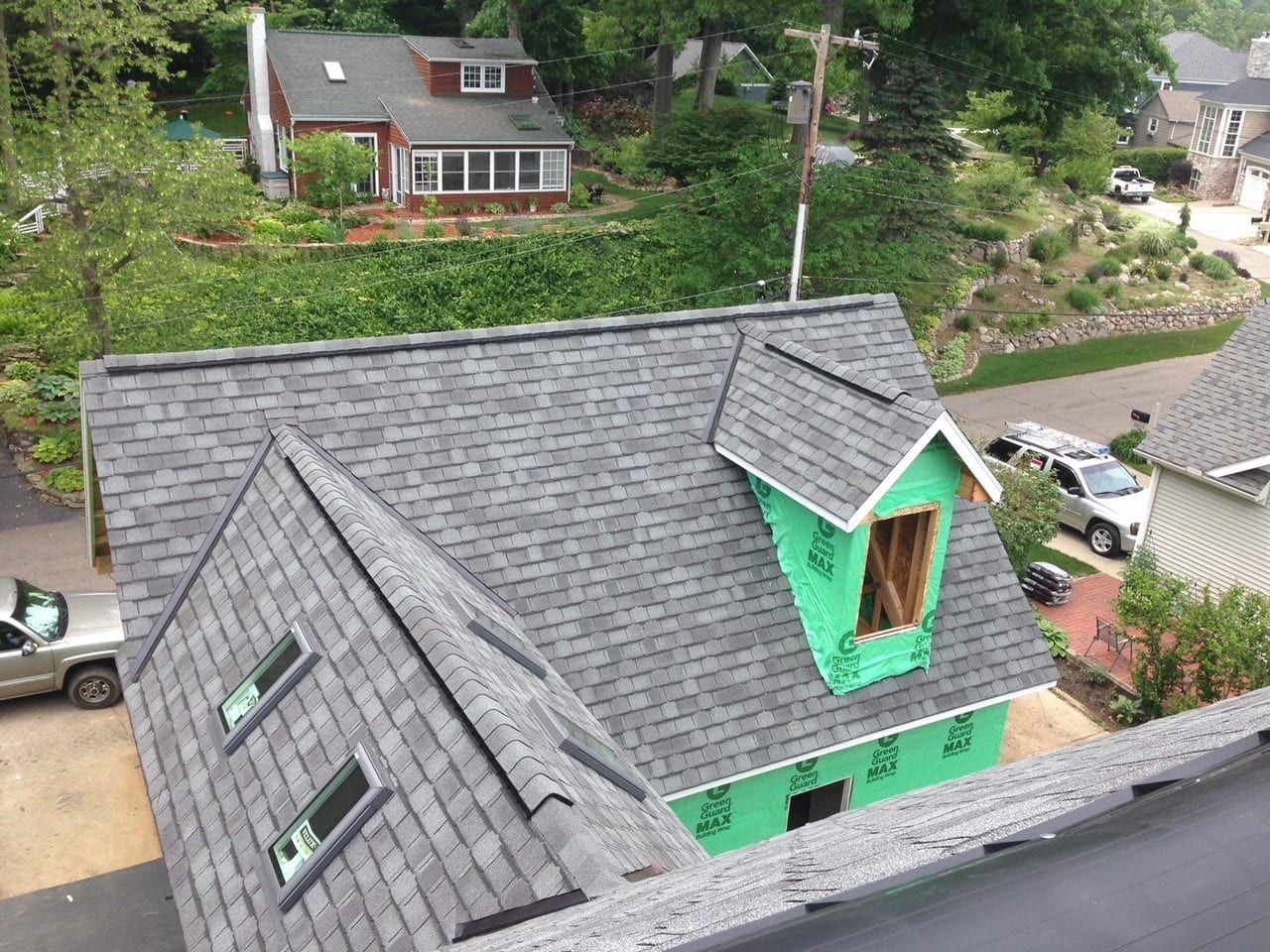 A high-angle view of a grey shingled roof under construction with two skylights and a green-sheathed dormer.