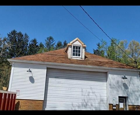 A white garage with a brown roof and a dormer window against a clear blue sky.