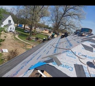 Workers installing roofing felt on the pitched roof of a building during a sunny day.