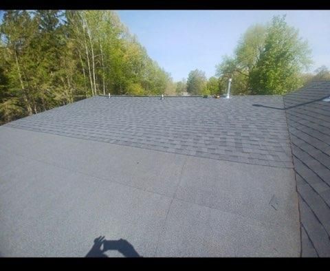 A high-angle view of a partially replaced residential roof, showing dark shingles installed above a grey flat roof base.