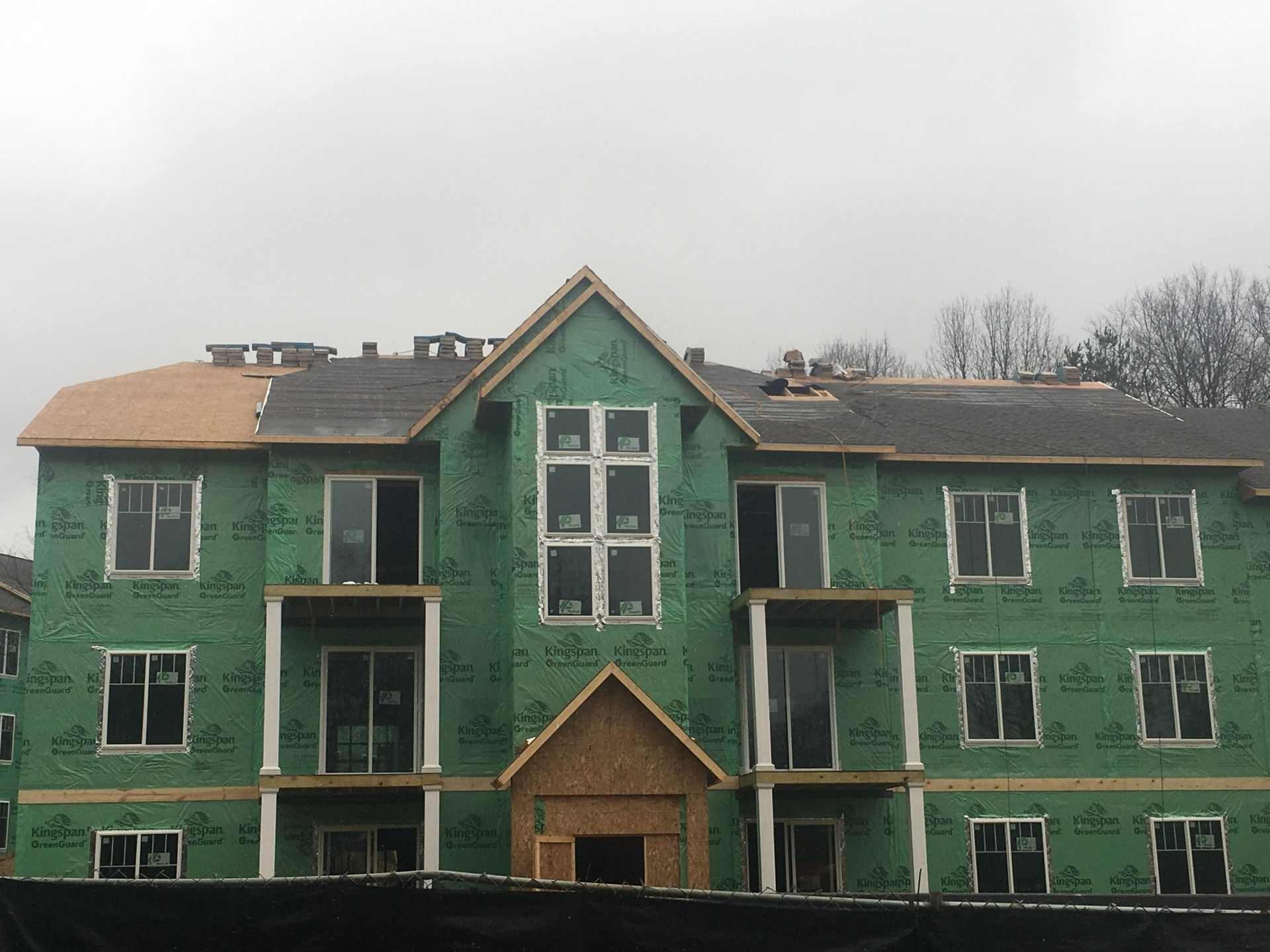 A multi-story apartment building under construction, featuring green sheathing, windows, and an unfinished roof.