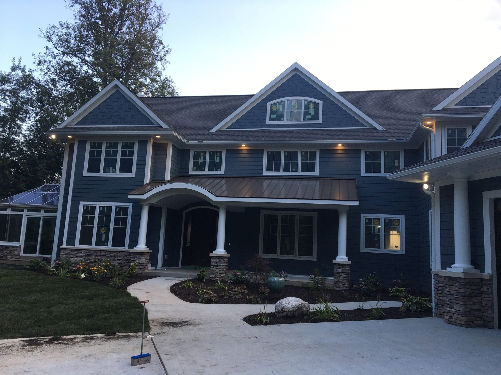 A large two-story house with blue siding, stone accents, a covered front porch, and a concrete driveway at twilight.