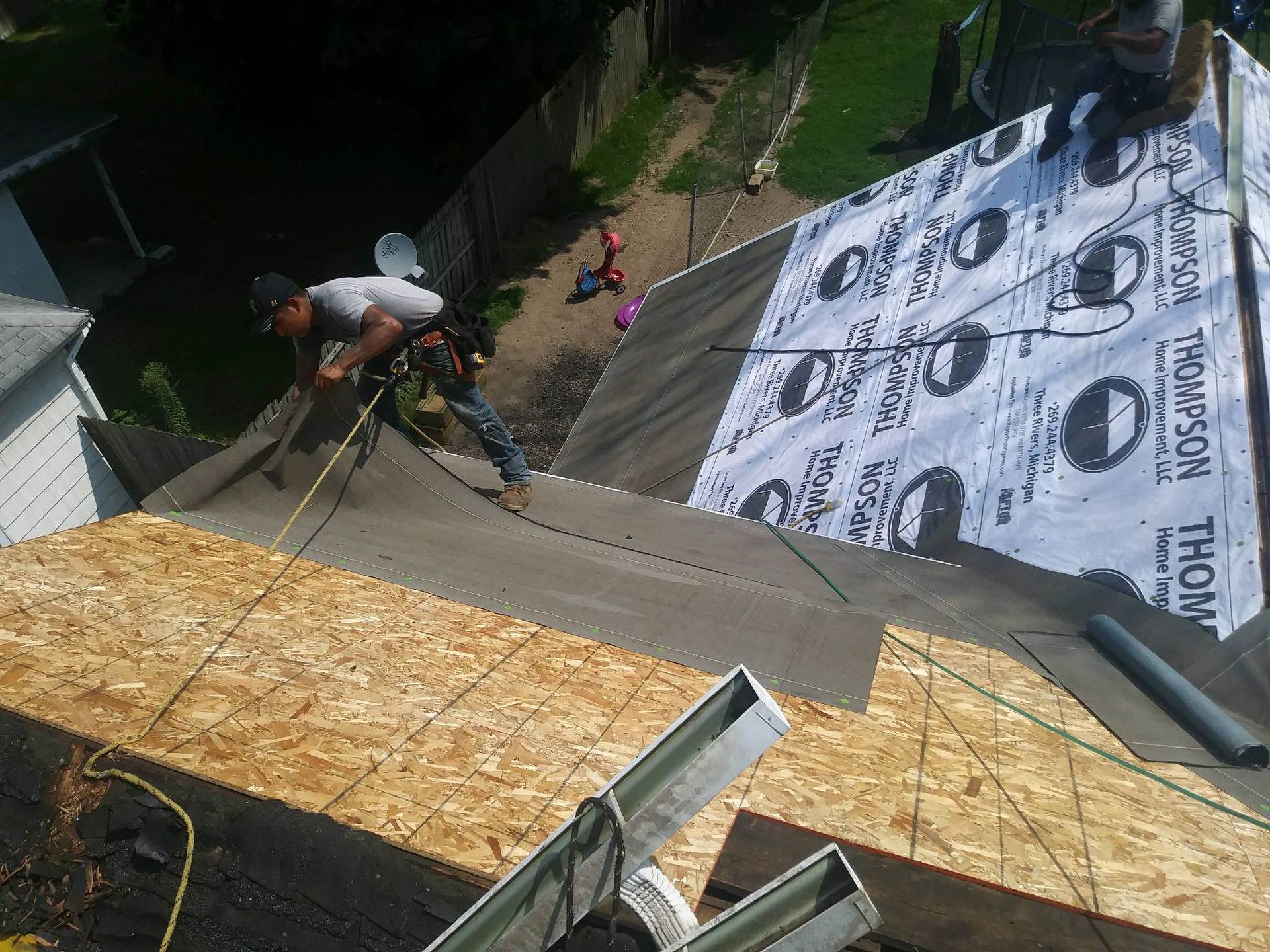 Workers install new roof decking and underlayment on a steep house roof.