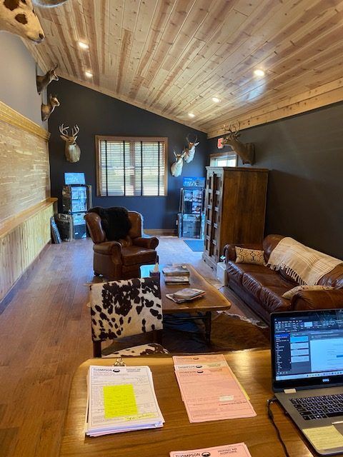 A rustic office space featuring a leather armchair, a brown leather sofa, a wood coffee table, and deer head wall mounts.