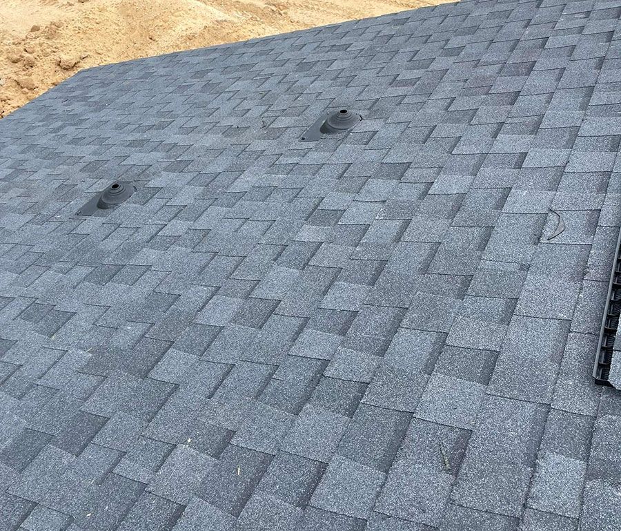 A close-up view of a dark gray asphalt shingled roof with two small, dark ventilation vents installed on the surface.
