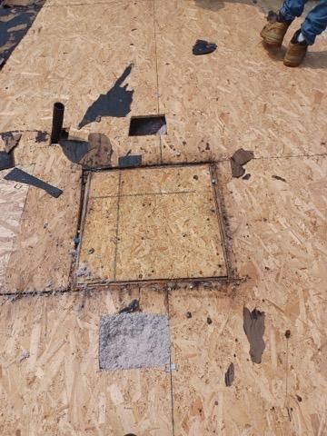 Roof deck showing a repaired square section of OSB sheathing with leftover roofing material and a nearby vent pipe.