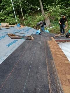 Two workers install shingles and underlayment on a residential roof.