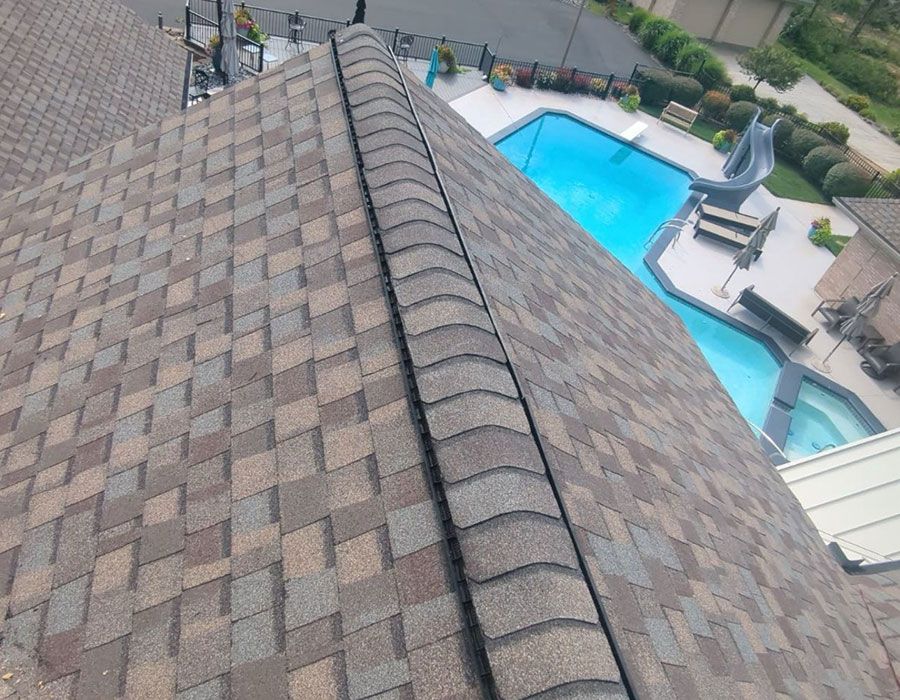 An aerial view of a textured, shingled roof sloping down toward a backyard swimming pool.