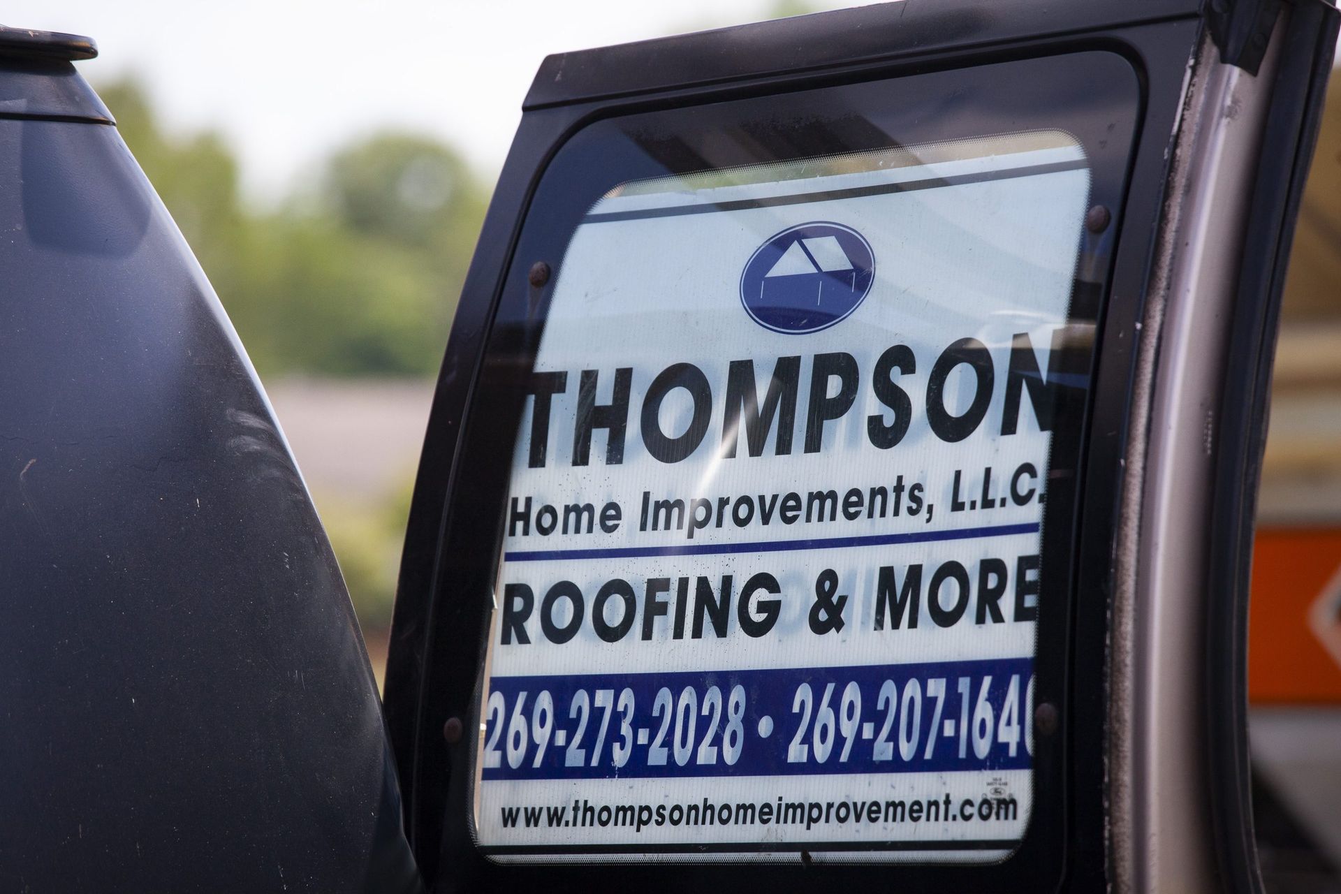 A decal on a vehicle window for Thompson Home Improvements, L.L.C., listing roofing services and two phone numbers.