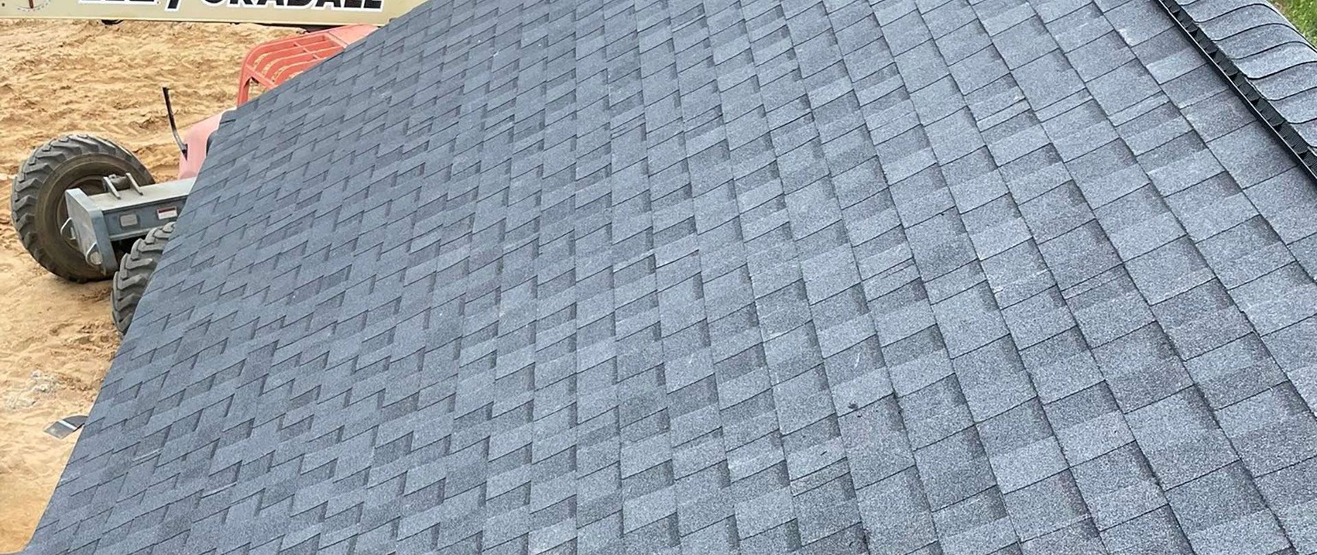 A close-up, angled view of a newly installed dark gray architectural shingle roof with a partial view of heavy machinery.