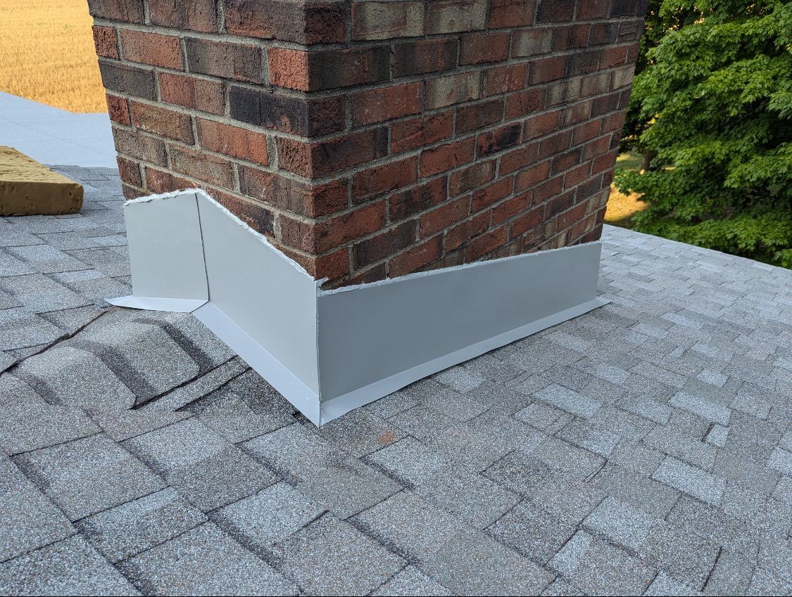 New grey metal flashing installed around the base of a brick chimney on a shingled residential roof.