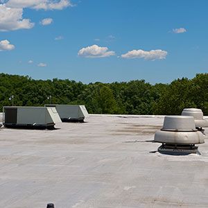 Two rectangular HVAC units and two circular roof vents sit on a flat gray roof under a blue, cloudy sky.
