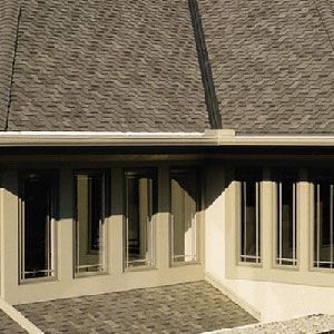 Exterior corner view of a building with light-colored stucco walls, tall multi-pane windows, and a dark shingled roof.