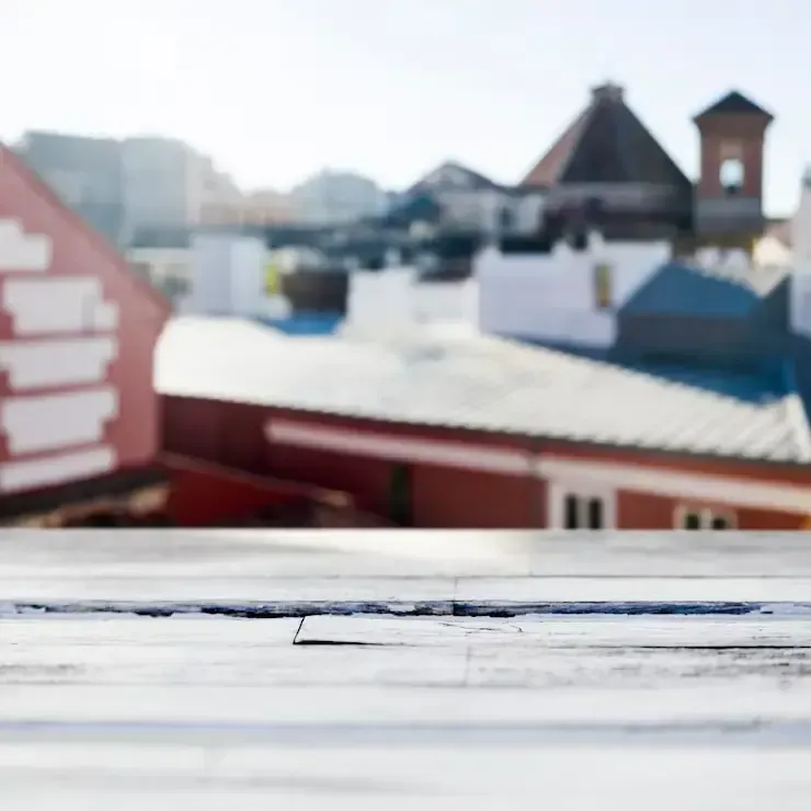 A white wooden surface in the foreground overlooking a blurred view of red and white buildings against a clear sky.