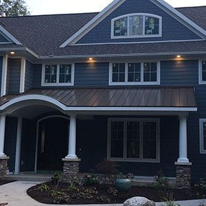 A two-story blue house with a covered front porch, dark metal roof, white trim, and a small garden in the front.