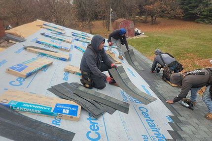 Roofers in work clothes installing dark asphalt shingles on a residential roof covered in CertainTeed underlayment.