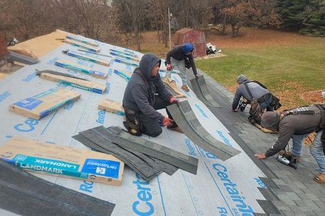 Four workers install shingles on a residential roof covered in protective underlayment.