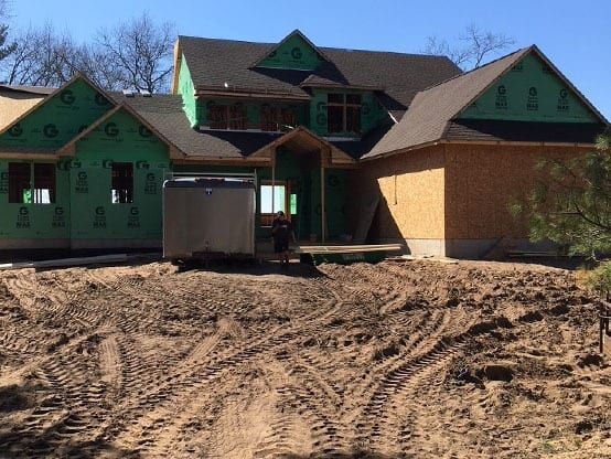 A new house under construction with a brown roof, green siding, and exposed wood framing, set on a dirt construction site.