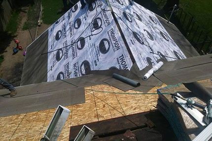High-angle view of a house roof undergoing repairs, showing plywood decking and partially installed underlayment.