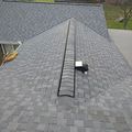 A high-angle view of a grey shingled roof featuring a long, black ridge vent running down the center of the peak.