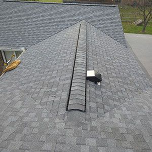 A high-angle view of a grey shingled roof featuring a long, black ridge vent running down the center of the peak.