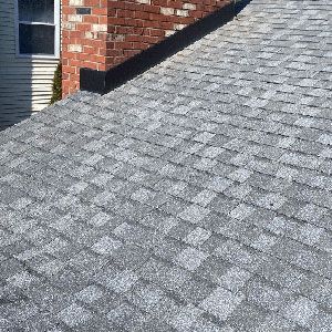 A close-up of a gray shingled roof meeting a brick chimney with black flashing.
