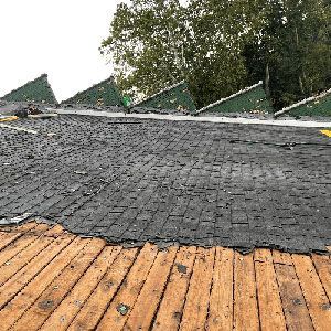 A roof under repair, showing exposed wooden slats in the foreground and a layer of black roofing material above.