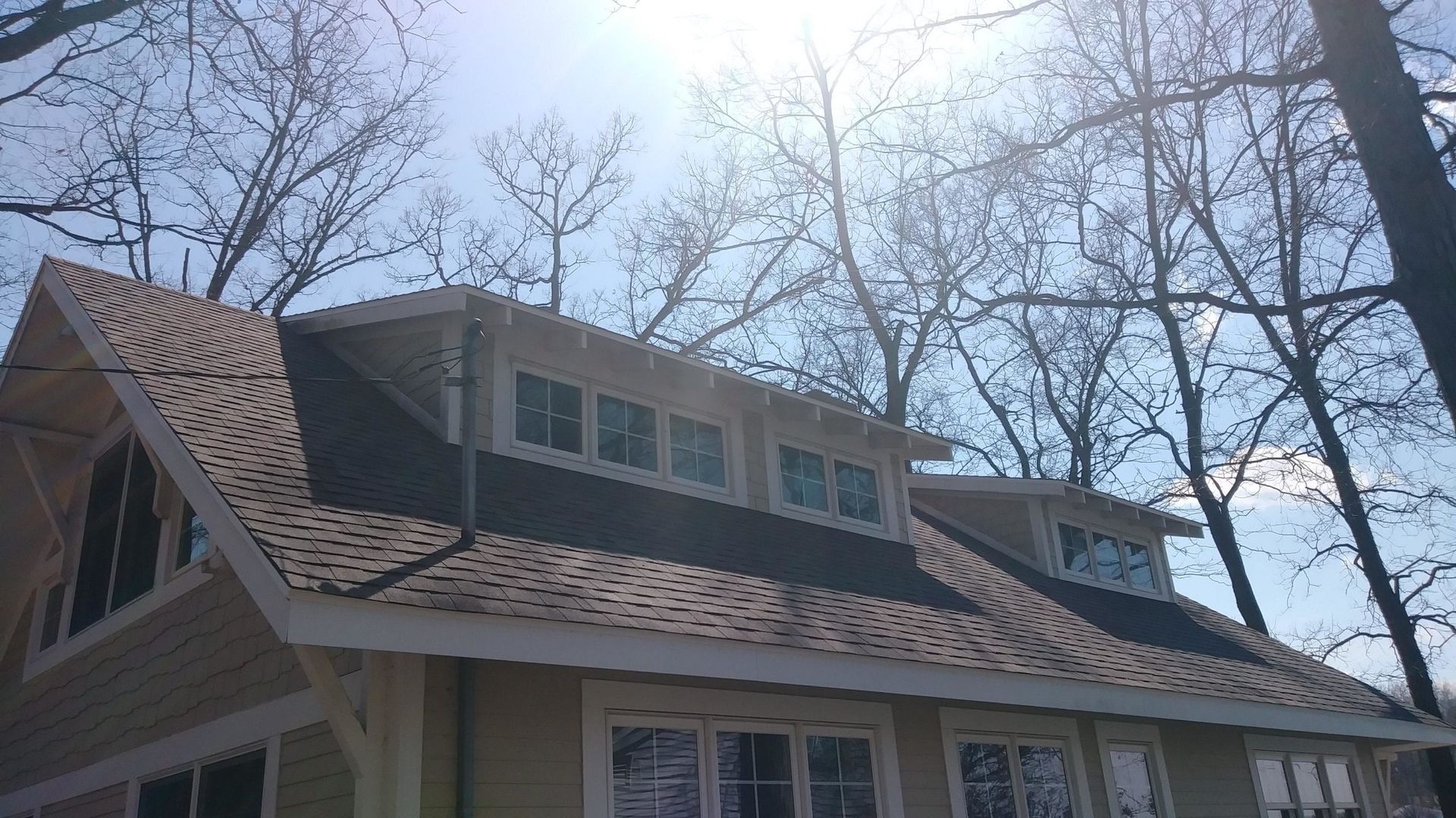A residential house under construction with light-colored siding, a partially shingled roof, and a dormer window.