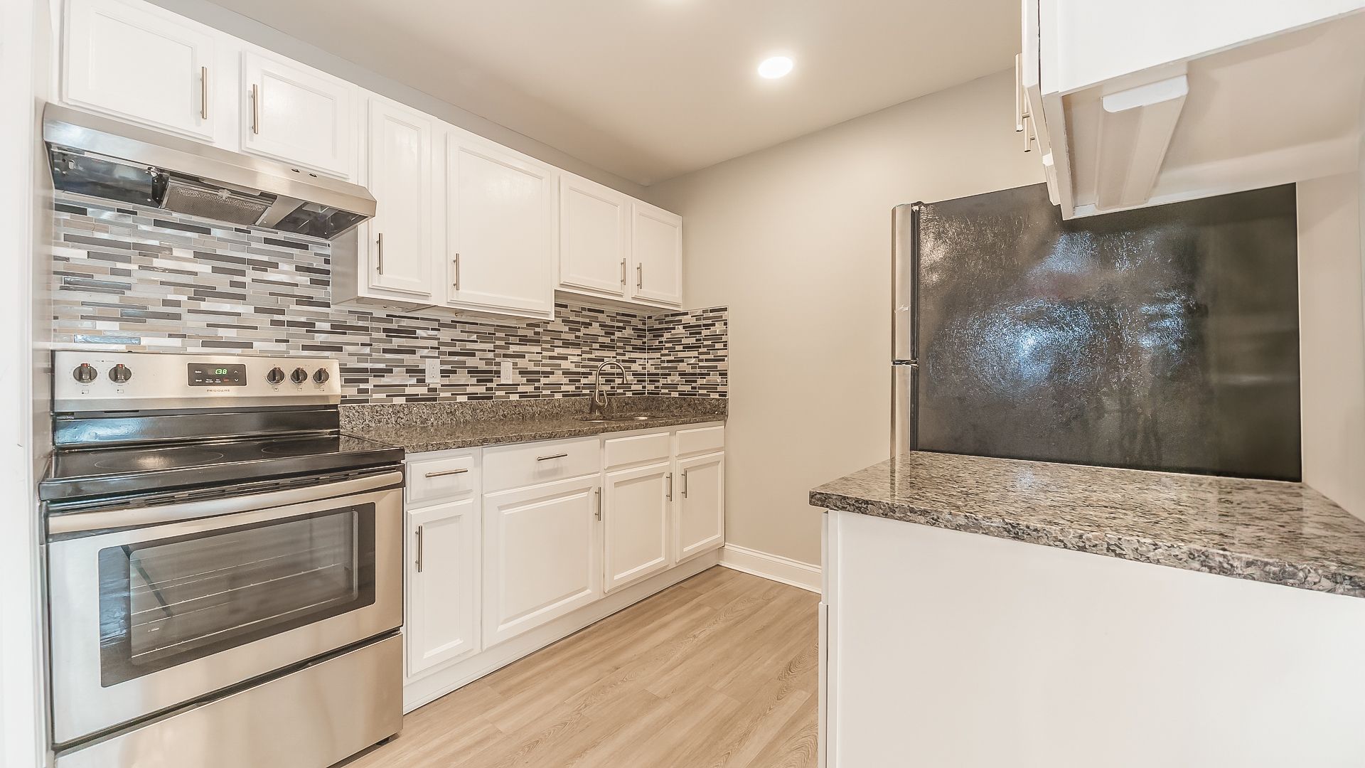 Modern kitchen with stainless steel appliances, white cabinets, and gray mosaic tile backsplash