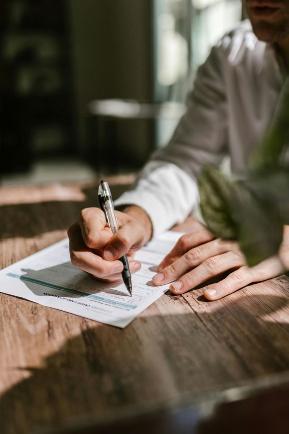 Person writing with a pen on a sheet of paper, close-up on hands and wooden table.