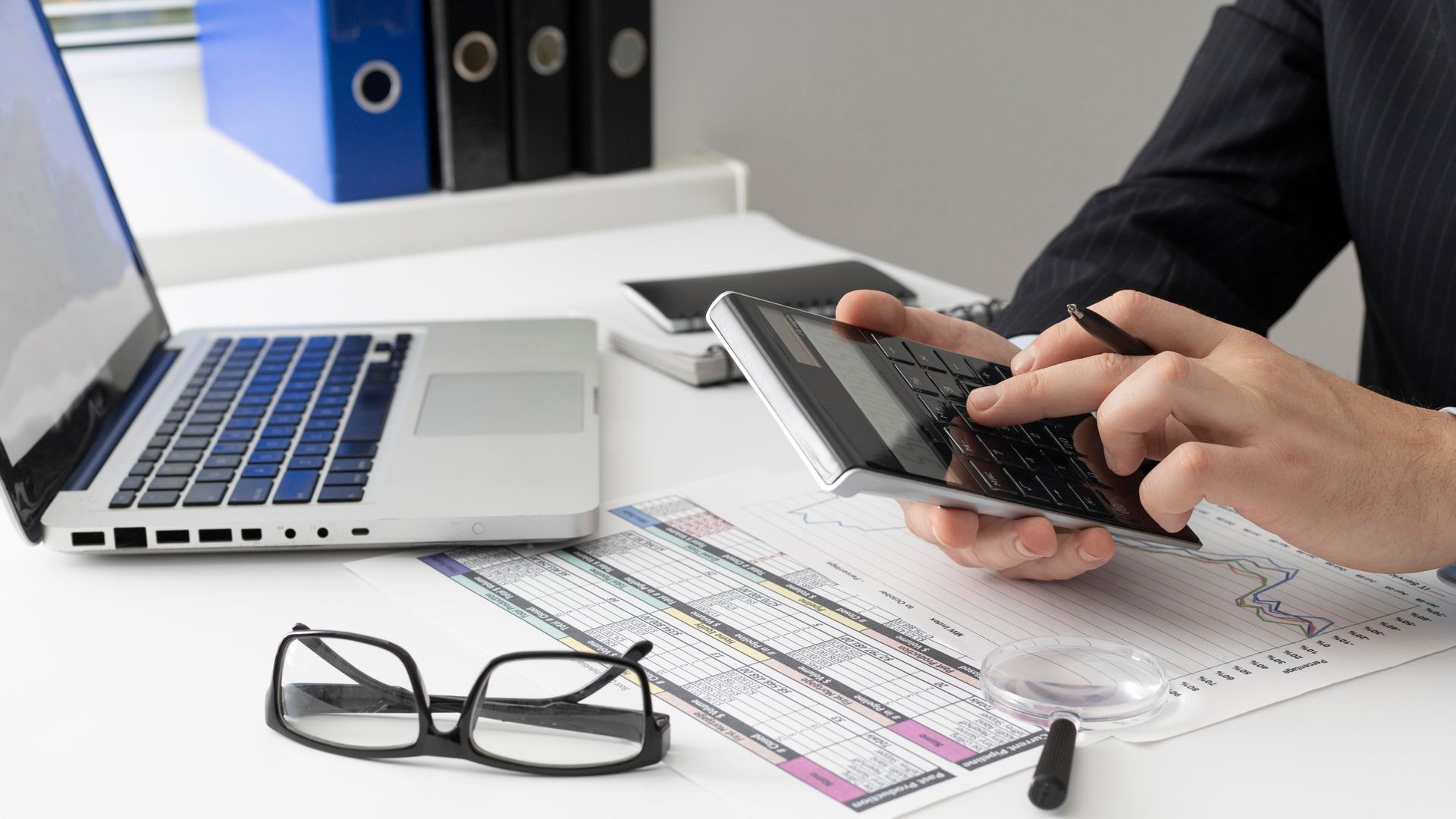 Person using a calculator on a wooden table; paperwork is visible.
