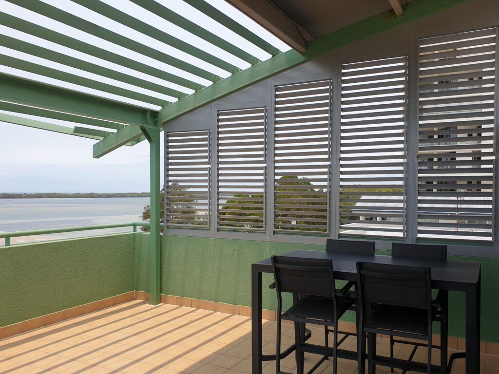 A Patio With A Table And Chairs And A View Of The Water — Balcony Shutters Australia In Moffat Beach, QLD