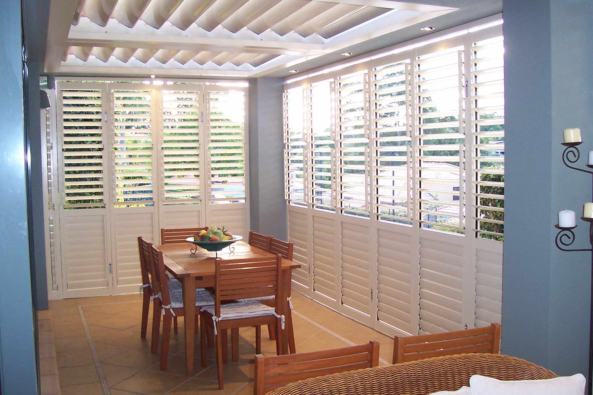 Outdoor patio dining area with timber plantation shutters surrounding a table and chairs.
