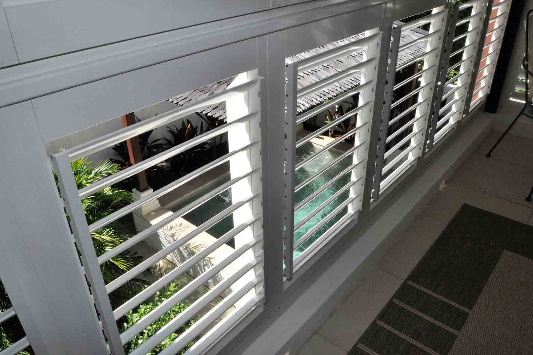 A Row Of White Shutters On A Balcony Overlooking A Pool — Balcony Shutters Australia In Moffat Beach, QLD