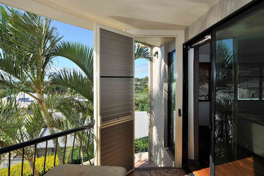 A Balcony With A View Of A Palm Tree And A Sliding Glass Door — Balcony Shutters Australia In Moffat Beach, QLD