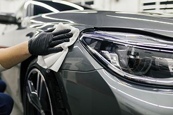 A person is cleaning a car with a cloth and gloves.