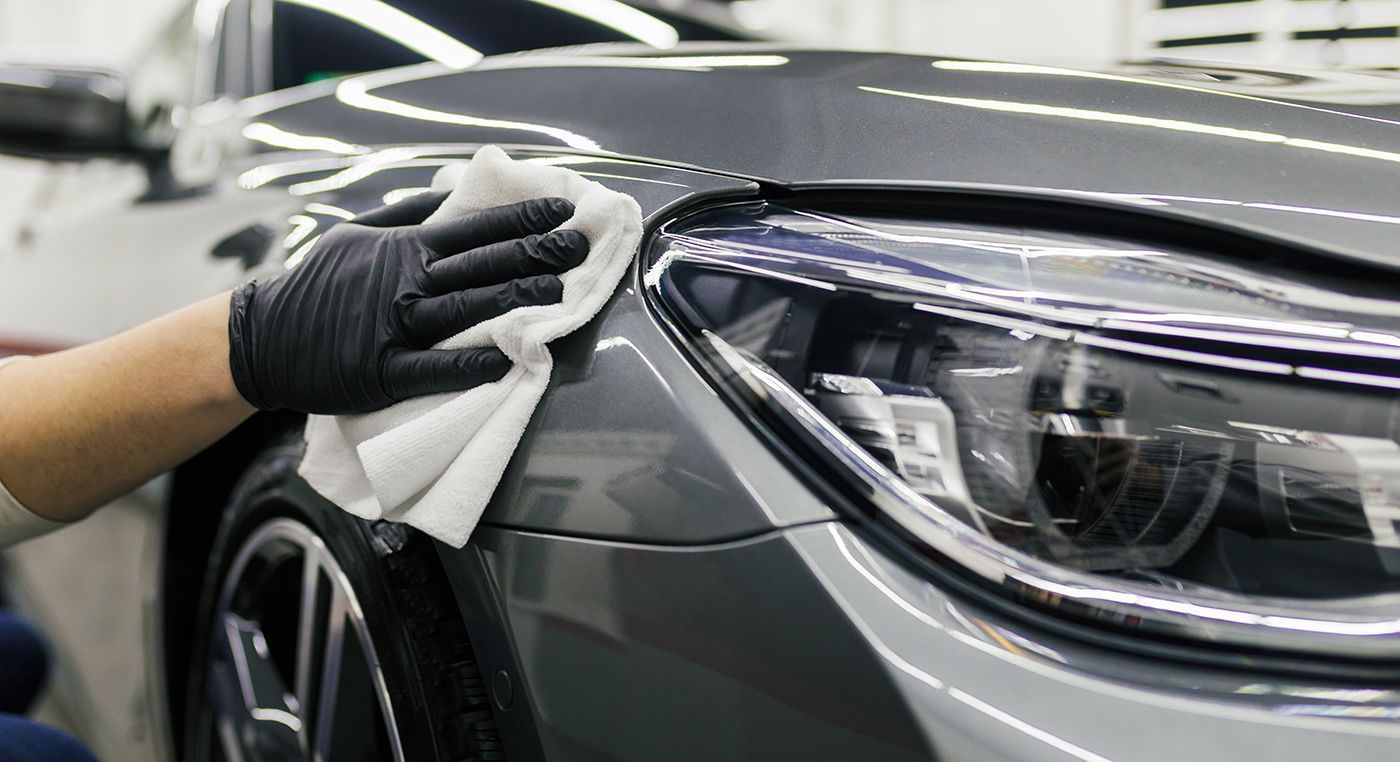 Gloved hand wiping a gray car's fender with a white cloth.