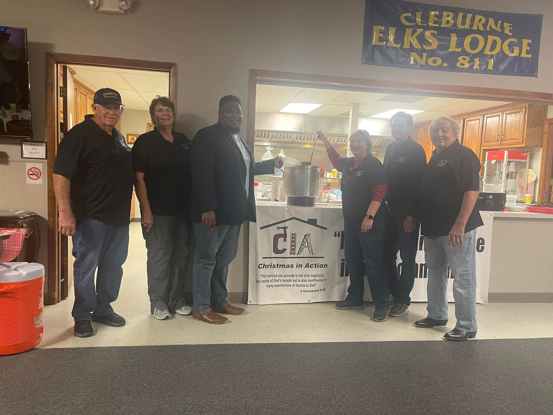 Six people posing outside the Elks Lodge No. 53 entrance, with a donation sign in front.