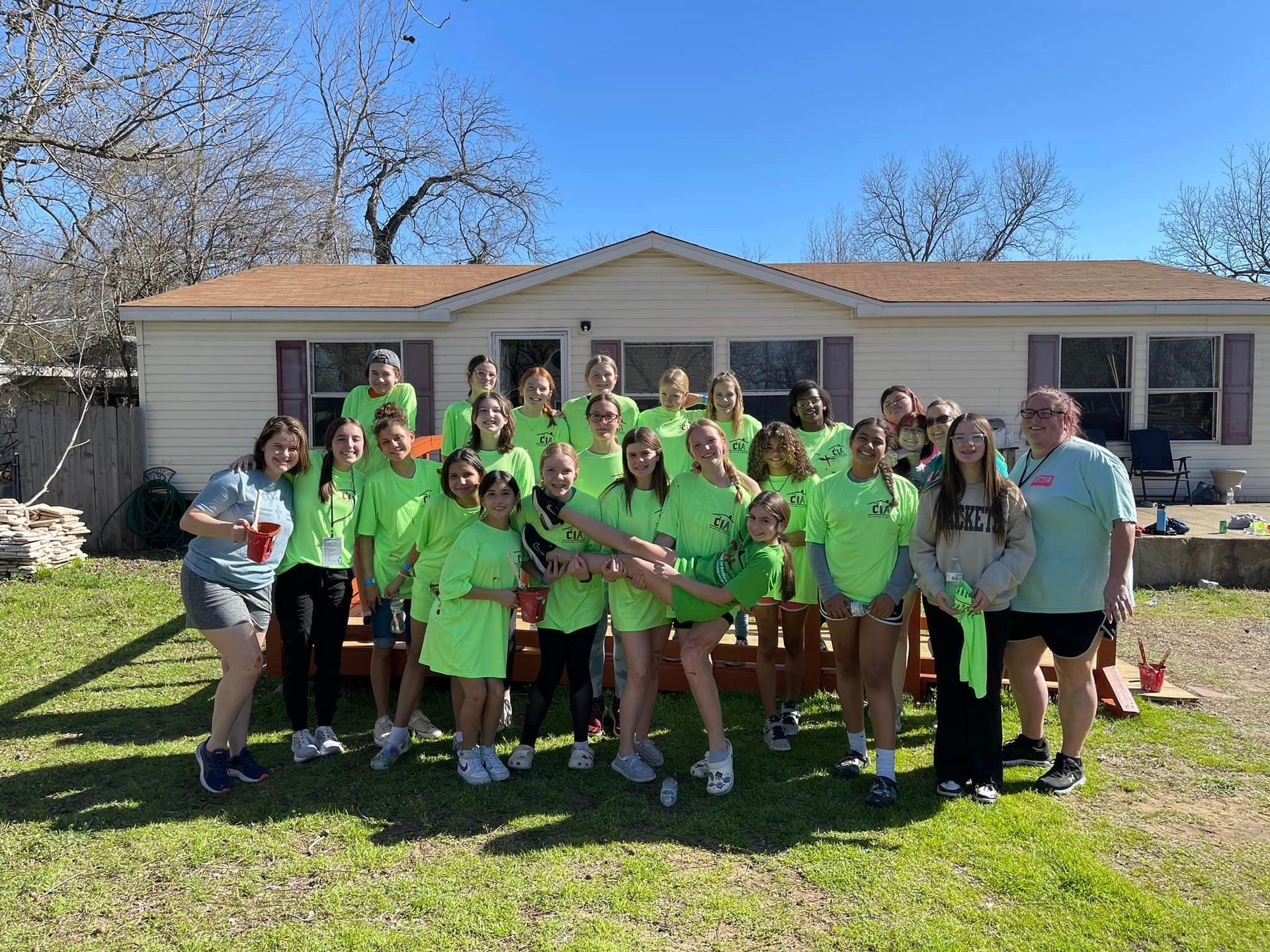 Group of people in neon green shirts posing outside a house on a sunny day