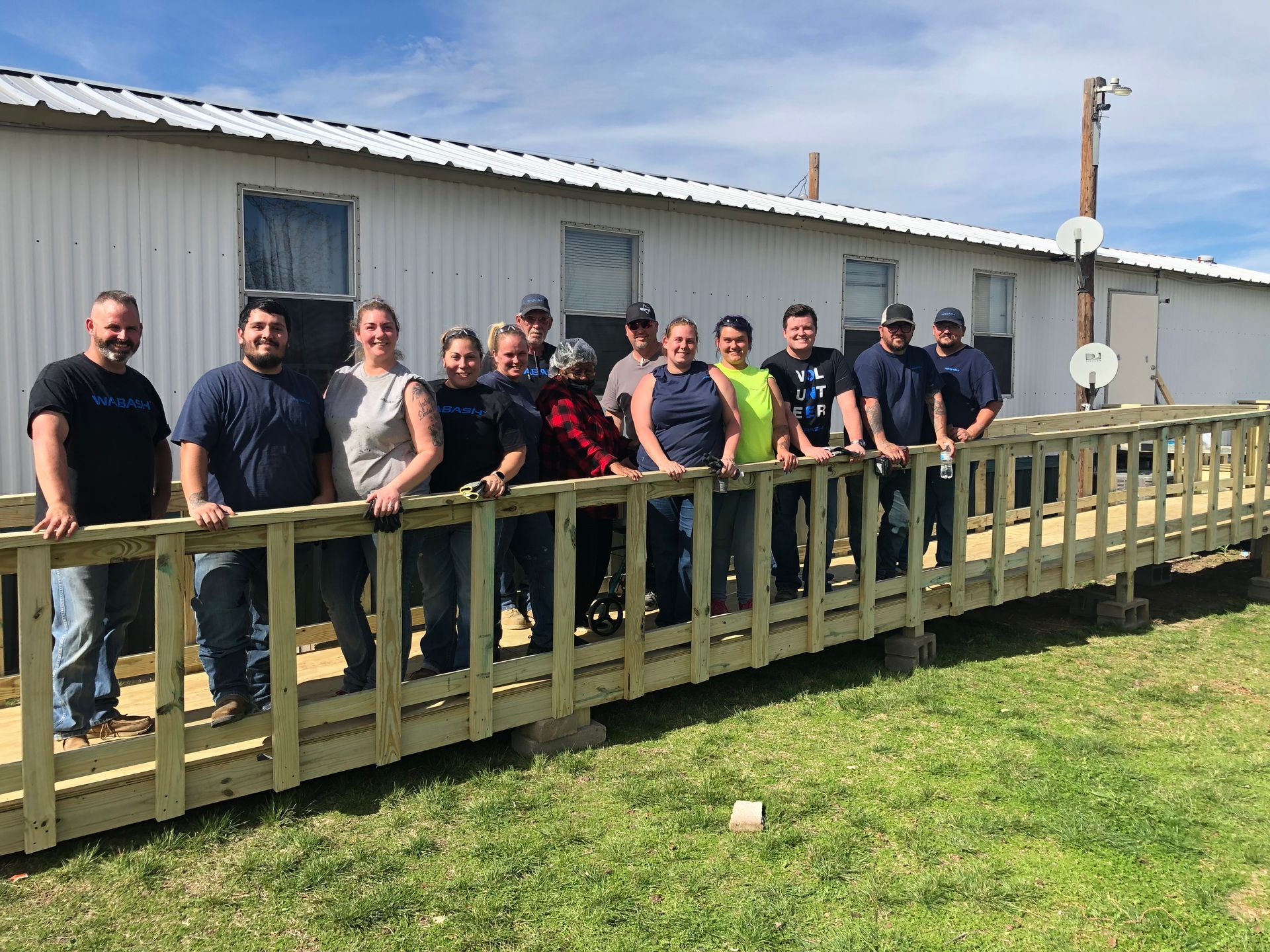 Group of people standing on a wooden ramp outside a white building on a sunny day