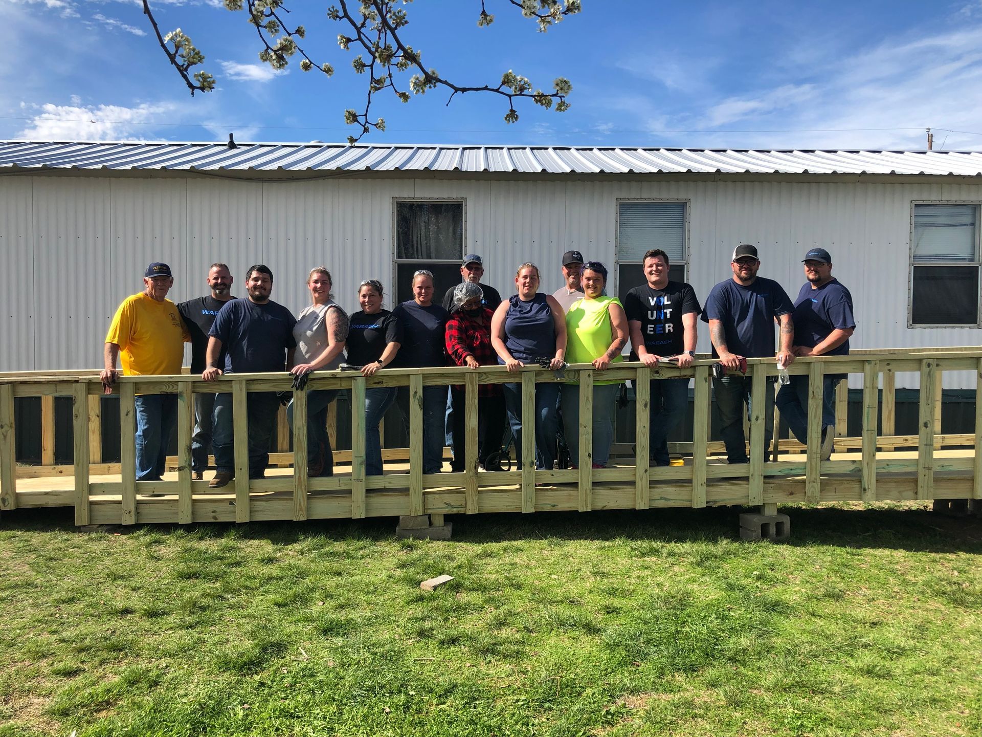 Group of people standing on a wooden deck in front of a white building on a sunny day