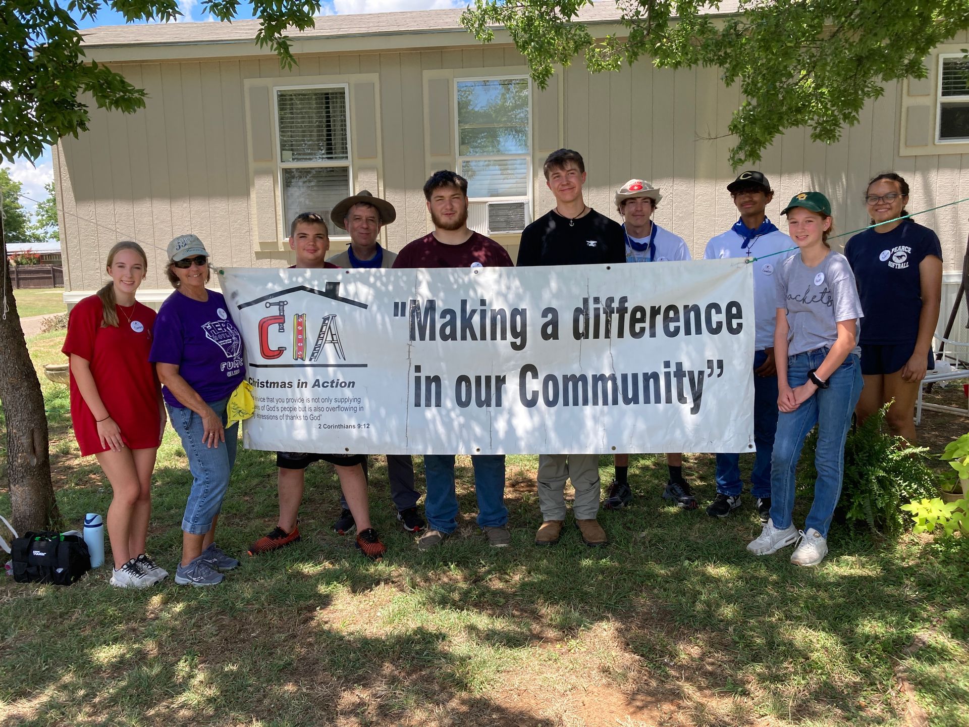 Group holding a banner reading “Making a difference in our Community” outside a house.