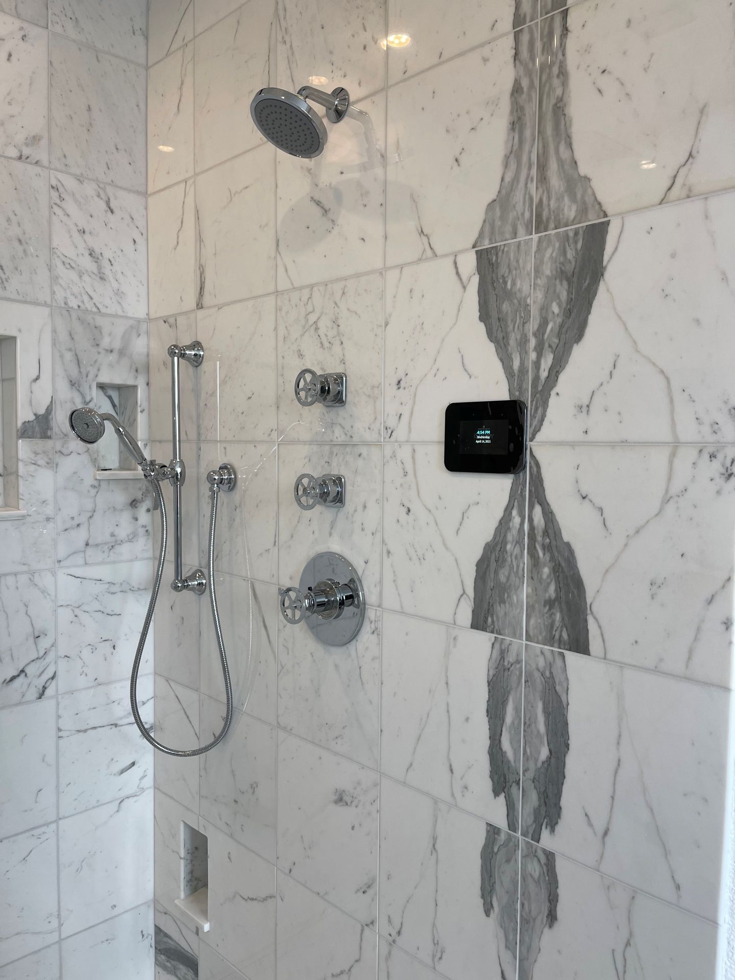 A modern tiled shower featuring a rainfall showerhead, handheld sprayer, temperature controls, and a digital display.