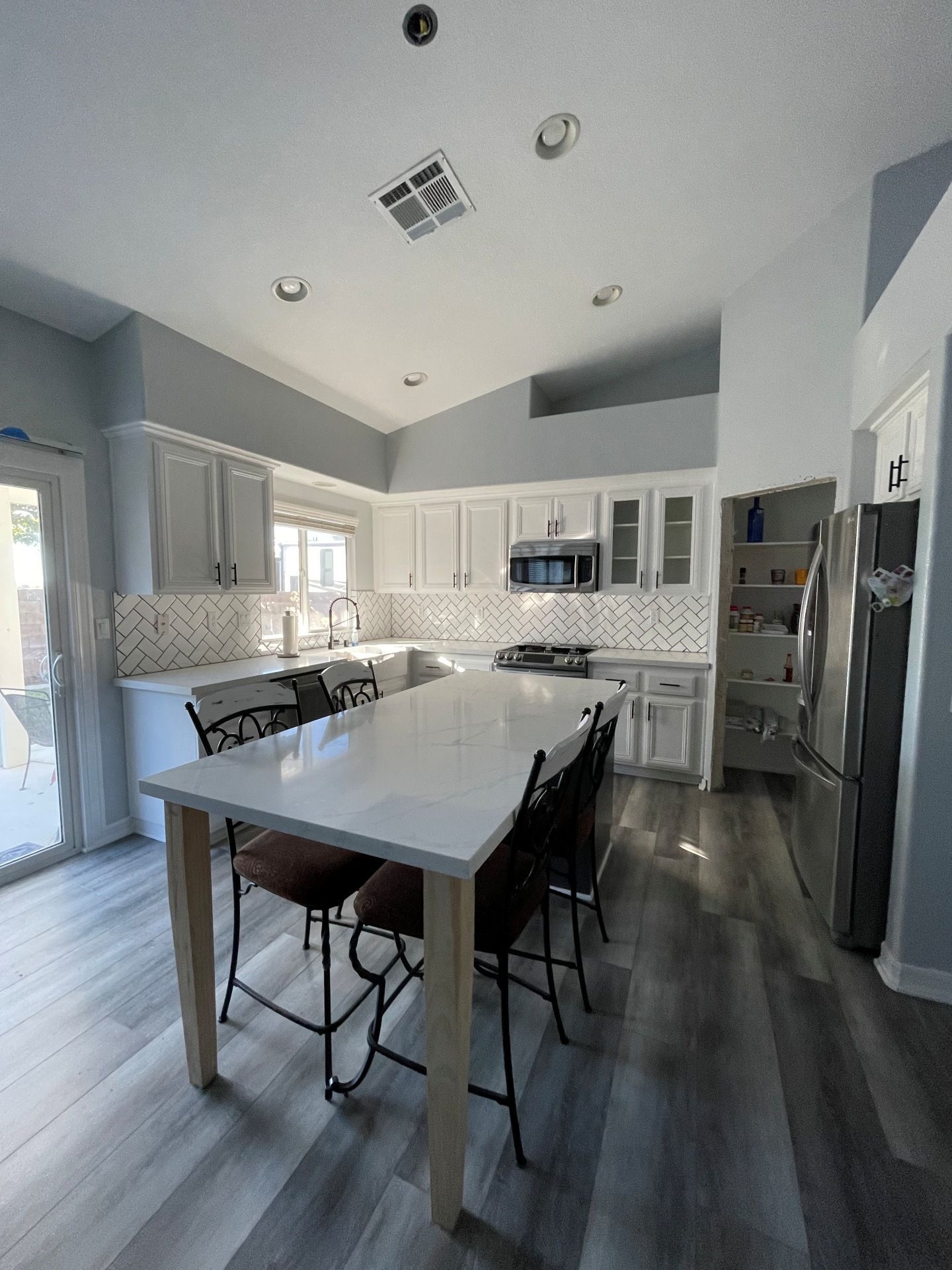 A modern, well-lit kitchen with a white quartz island, high stools, grey cabinets, and wood-toned floors.