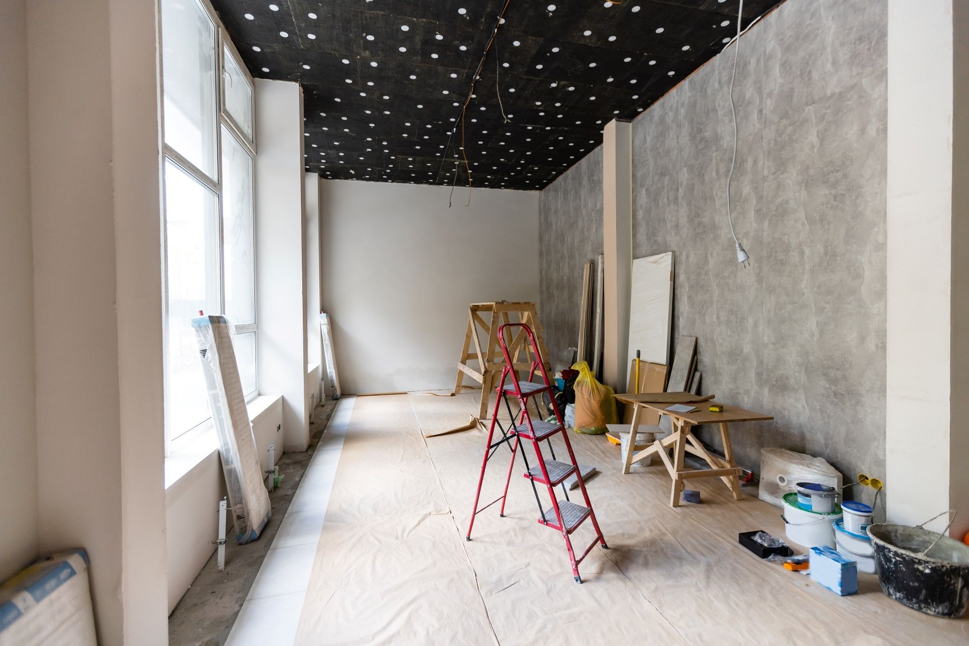 A renovation project in a narrow room with a black, star-patterned ceiling, grey textured walls, and a red step ladder.