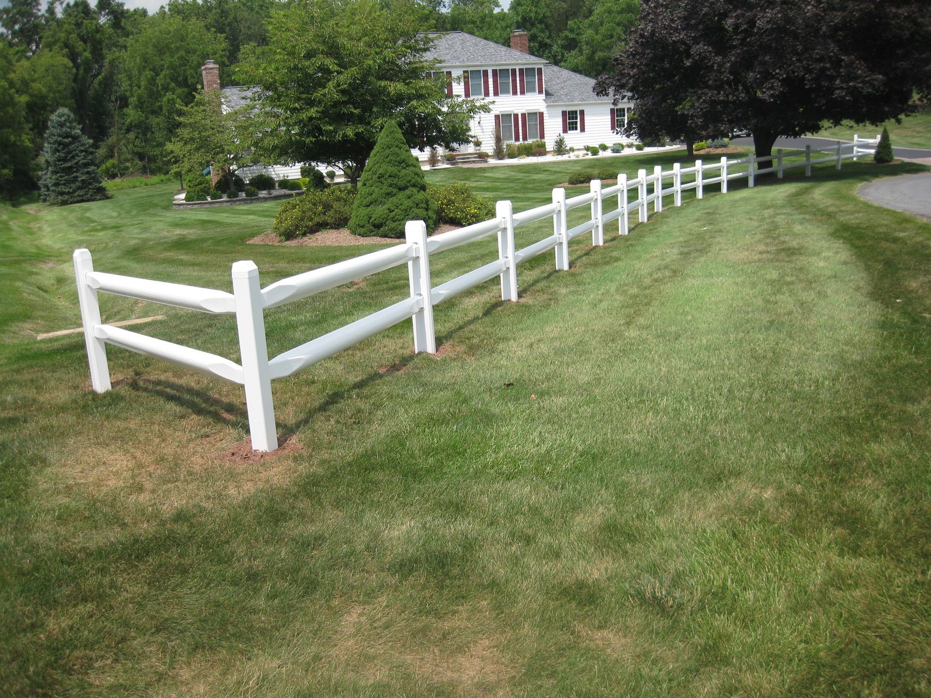 A white fence surrounds a lush green yard in front of a house