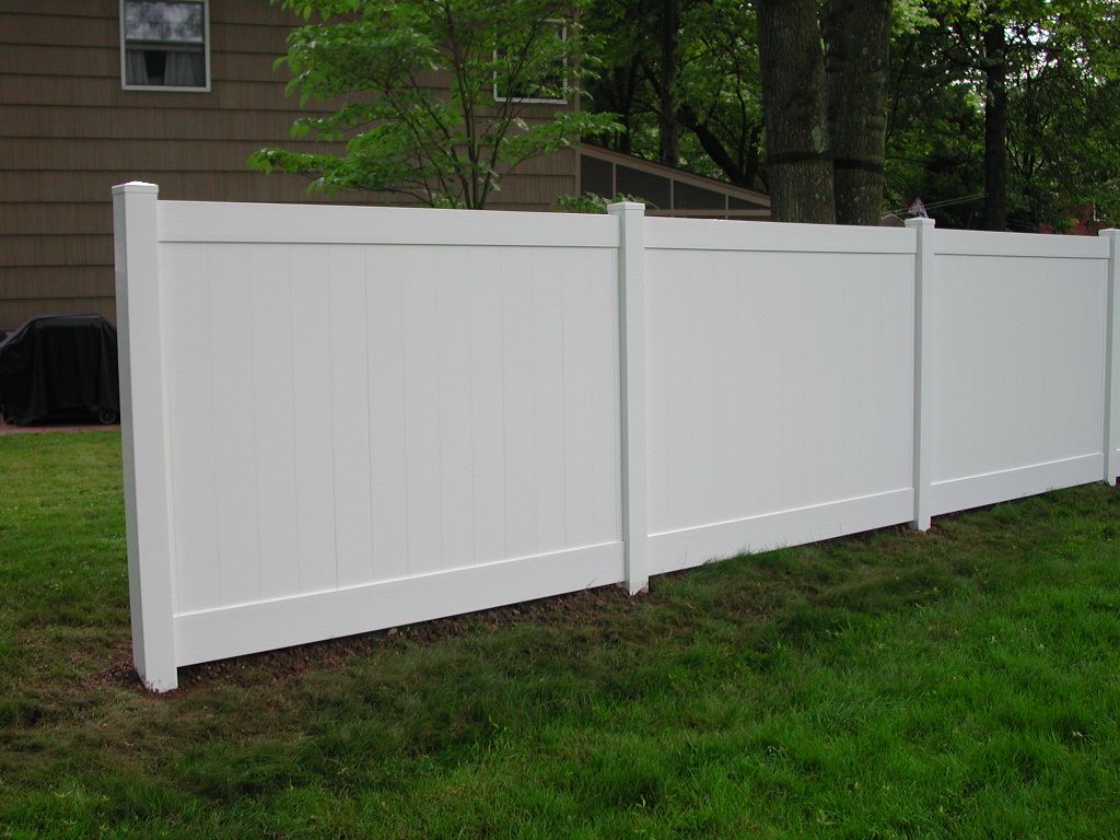 A white vinyl fence is sitting in the grass in front of a house.