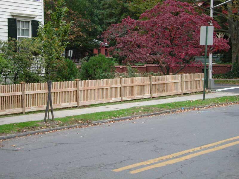A wooden fence is along the side of a street next to a house.
